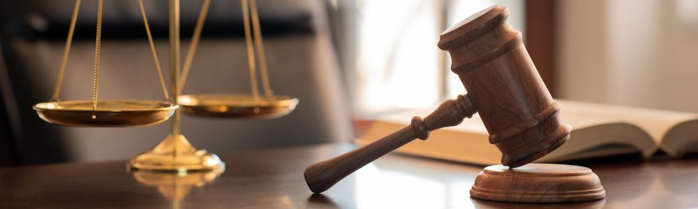 Atrybuty prawnicze – młotek sędziowski i waga szalkowa na tle otwartej książki. Grafika na bloga omawiająca zagadnienia prawne: egzekucja komornicza, obowiązek komornika oraz sytuacje, w których komornik ma prawo zająć konto osobiste dłużnika.